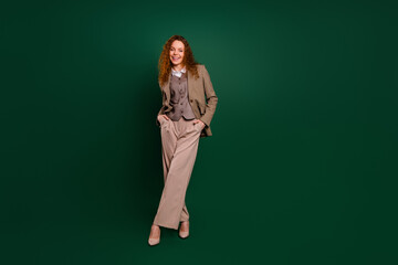 Professional young woman in stylish formalwear posing against an emerald green backdrop exuding...