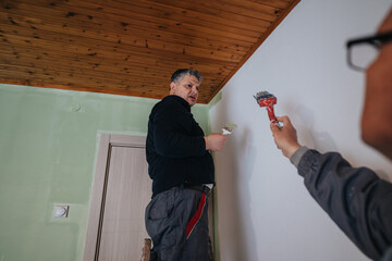 Two people collaborate to paint a room indoors, emphasizing teamwork and renovation efforts. The...