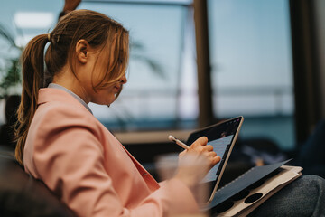 Focused woman sketching on a digital tablet with a stylus in a contemporary setting, showcasing...