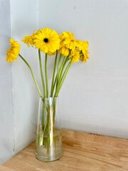 A clear glass vase with bright yellow flowers placed as a decoration on a table; suitable as home or café décor, home decor, or home decoration, interior, exterior