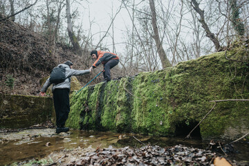 Hikers cooperating to traverse an overgrown, mossy structure in a forest, showcasing teamwork,...