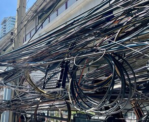 The black electrical wires on utility poles along the streets are tangled and installed in a...