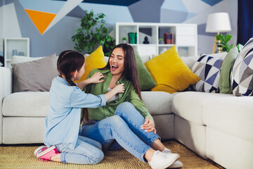 Young mother and daughter bonding playfully on a cozy sofa in a colorful modern apartment, sharing...