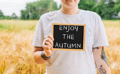 Woman holding a chalkboard with the words enjoy the autumn written on it