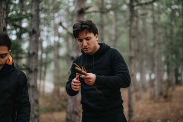 Two individuals in casual clothing gather sticks in a tranquil mountain forest, preparing for outdoor activities on a winter day.