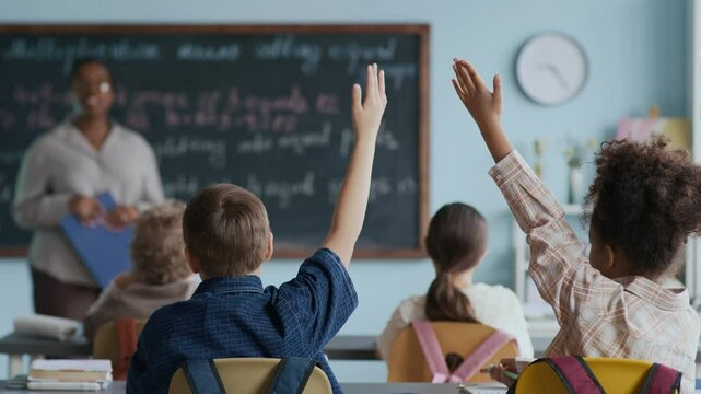Back view shot of two engaged young students raising their hands to ask or answer during interactive Math lesson with modern Black female teacher standing near chalkboard - Powered by Adobe