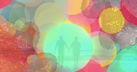 Walking senior couple holding hands on shallow sandy shore, with translucent circles over sea waves