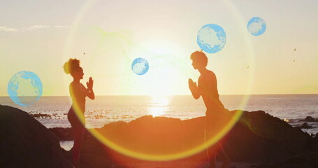 Practicing couple in activewear holding prayer pose on rocky outcrop at sunset, with ocean backdrop