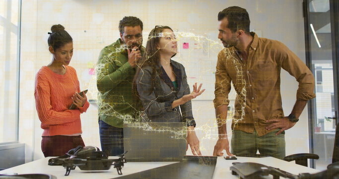Analyzing team in business attire viewing holographic map in office, with drones and VR headset