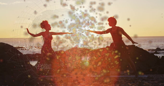 Dance duo performing mirrored yoga pose on rocky beach at sunset, with yoga mats, bokeh overlay