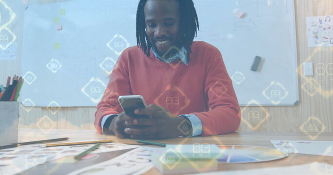 Smiling mid adult designer holding smartphone at modern design studio, with pencils and 6G overlay