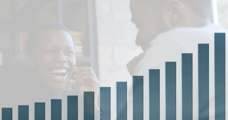 Laughing business professionals discussing sales figures at desk, with smartphone and bar chart