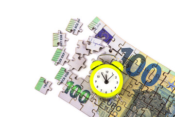 A 100 euro note made from puzzle pieces and an alarm clock on a white background