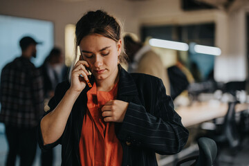 A professional woman in a busy office discusses important matters on her phone. She appears...