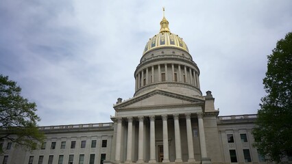 Visitors admire the stunning architecture of the West Virginia State Capitol in Charleston, showcasing its iconic golden dome and classical columns against a cloudy sky.