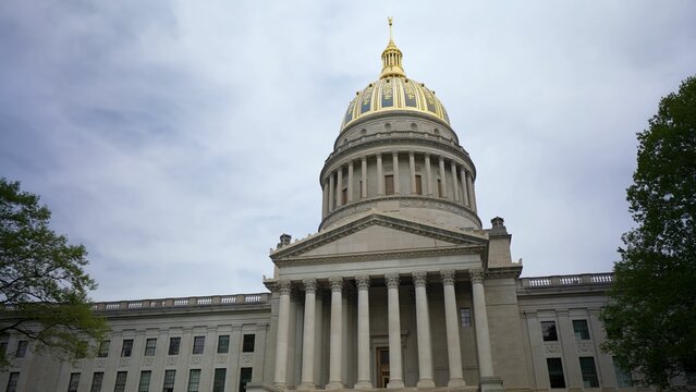 Visitors admire the stunning architecture of the West Virginia State Capitol in Charleston, showcasing its iconic golden dome and classical columns against a cloudy sky. - Powered by Adobe