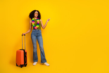 Stylish young woman with colorful accessories holding luggage on vibrant yellow background, ready...