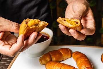 close-up horizontal photo of adult male hands opening whole wheat empanada with pineapple inside, whole wheat cheese sticks, next to cup of coffee in a healthy vegetarian restaurant in Colombia.
