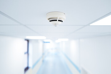 Shallow focus of smoke detection seen within a ceiling along a typical NHS hospital in Britain. The corridor branches to various wards.