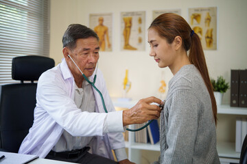 Obraz premium Senior male doctor using a stethoscope to examine a young female patient in a clinic. Health care concept.
