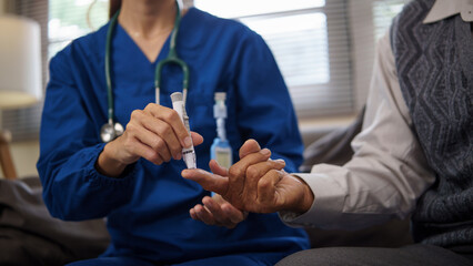 Home caregiver using lancet to check blood sugar levels of older patient. Health care concept.