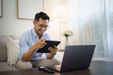 Smiling man using a digital tablet while working remotely from his cozy living room.