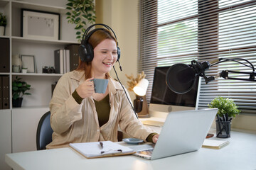 Young woman hosting a podcast from home, speaking into a microphone with coffee in hand.