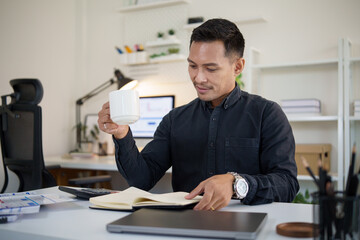 Businessman enjoying coffee while reading a notebook at his modern desk.