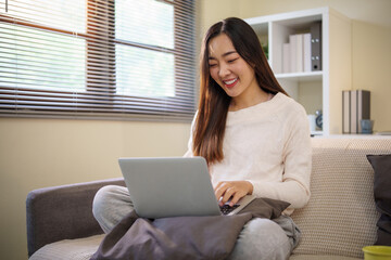Smiling woman using laptop at home with natural light through window blinds.