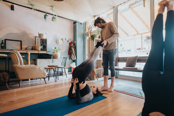 An instructor assists students during a yoga session in a cozy, creatively designed indoor space...