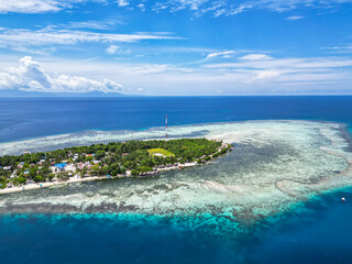 Fototapeta premium Picturesque Tropical Island with Village and Jetty Surrounded by Clear Blue Waters and Coral Reefs in Indonesia