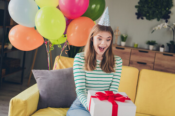 Young woman excitedly receiving a gift while celebrating in a colorful party setting with balloons...