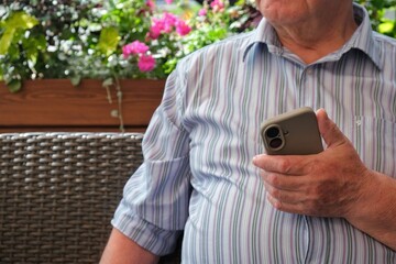 An elderly man is talking on a mobile phone near a cafe. A pensioner with a smartphone. A close-up of an elderly man holding a modern smartphone
