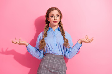 Young woman in glasses with braids in blue shirt expressing uncertainty on pink background indoors