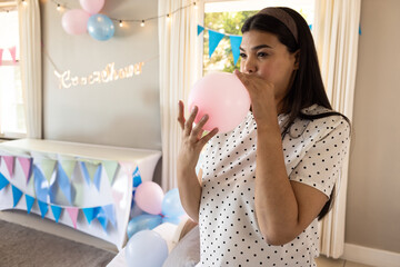 Woman in polka dot blouse inflating pink balloon under baby shower banner in room, copy space