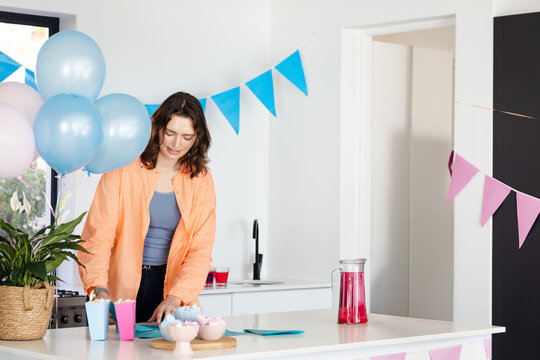Woman arranging pastel pennant banners and placing candy bowls with drink pitcher on kitchen island