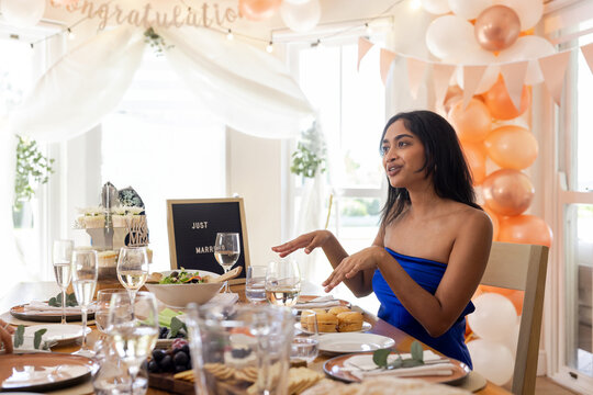 Indian bride in blue formal dress gesturing toward wedding cake at wedding reception, copy space