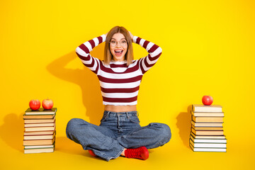 Excited young woman in a striped sweater sitting cross legged with book and apples on a vibrant...