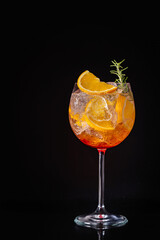 Aperol spritz cocktail in a glass with ice and orange on a black background