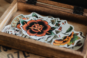 Close-up of wooden box filled with vintage-style rose tattoo flash stickers showcasing orange and...