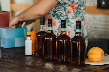 Bartender arranging amber spirits bottles on rustic wooden bar top beside fresh orange and mixer...