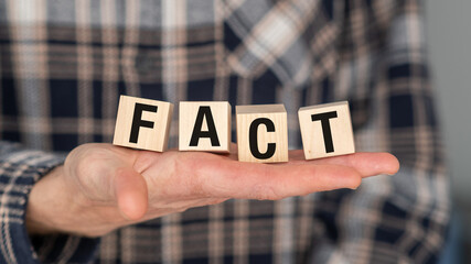 A person is holding a wooden block with the letters FAC on it