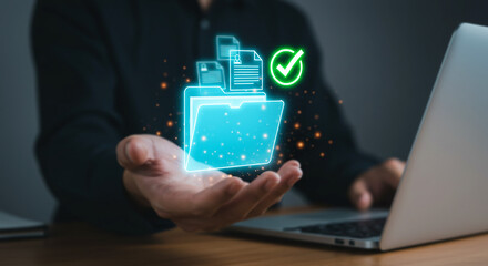 Data Security Concept: A person's hand gently cradles a glowing digital folder icon with a checkmark, symbolizing secure data storage and successful file management. A laptop rests nearby.
