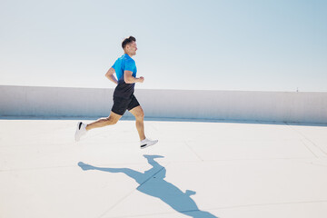 Bright daylight captures a man running on a road with clear skies above, showcasing urban fitness...