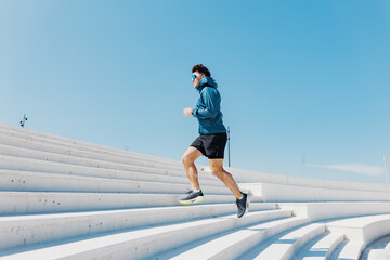 Man runs energetically up the stairs in a bright blue sky during a sunny day, showcasing athletic...