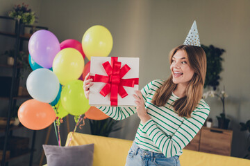 Young woman celebrating indoors holding a gift box with a cheerful smile during a colorful birthday...