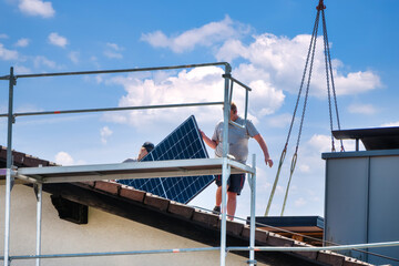 Two roofers dismantle solar panels and prepare them for crane transport
