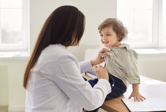 Pediatrician, medical doctor care of infant, children, female healthcare professional, wearing white medical coat examining small boy during medical visit in clinic office, hospital check up