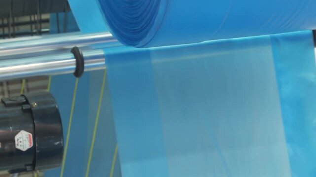 Automatic plastic bag making machine with lighting effect. Close-up of rotating roller of plastic bag making machine in light blue scene. Product packaging concept