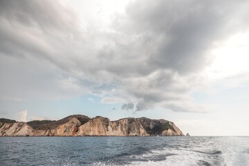 Cliffs tower majestically over calm waters, reflecting hues of a setting sun. Dark clouds loom...